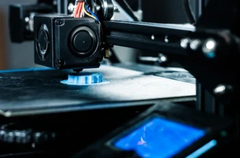 Uma impressora 3D criando uma peça plástica azul camada por camada.